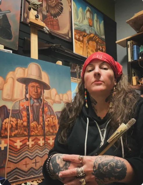 Sara  Bloodwolf in Studio with her paintings and brushes in hand.
